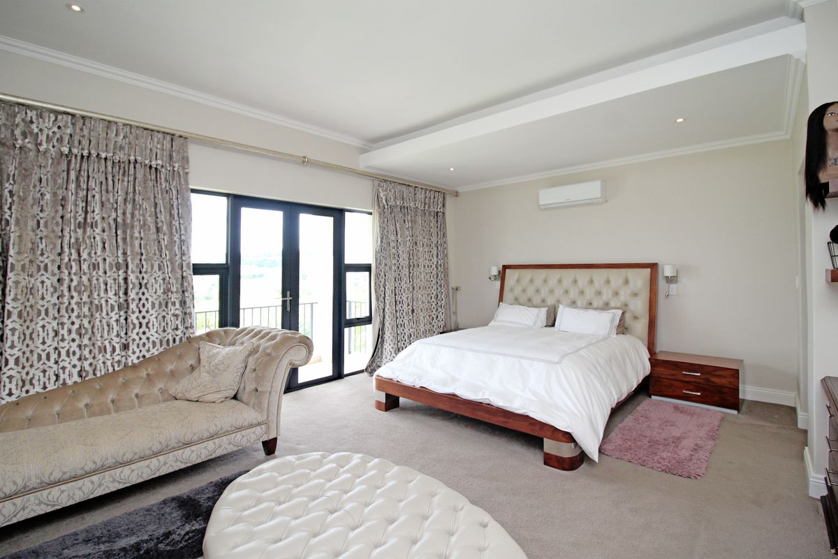 Spacious bedroom featuring a tray ceiling, recessed lighting, wall-mounted air conditioning unit, and large glass sliding doors leading to a private balcony.