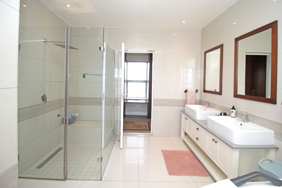 Modern bathroom featuring a double vanity with vessel sinks, a large walk-in glass shower, and polished floor tiles.