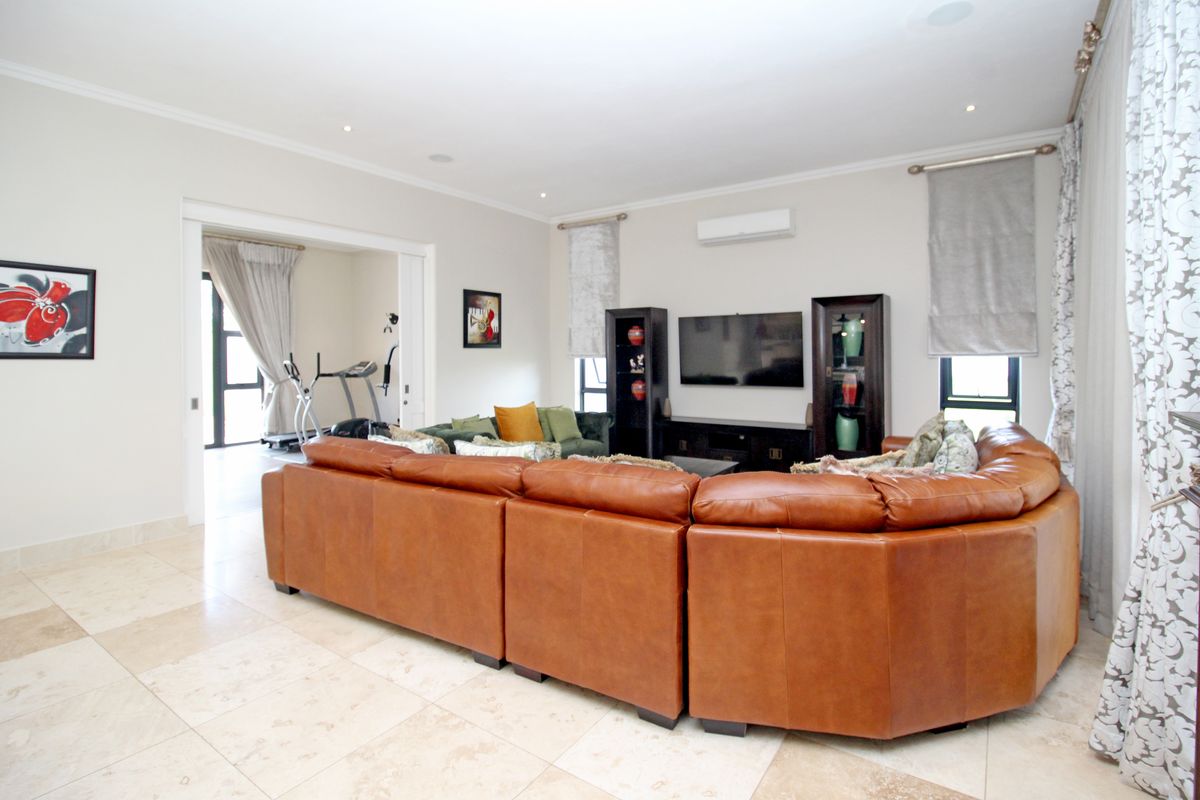 Spacious living room featuring large format floor tiles, recessed downlighting, and a wall-mounted air conditioning unit, with an adjacent room visible through sliding doors.