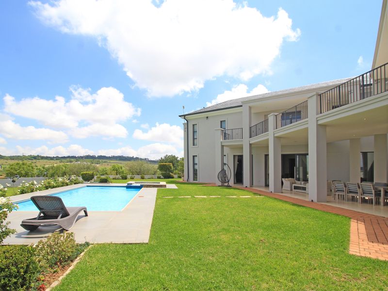 Rear view of the property featuring a swimming pool, landscaped garden, and a spacious covered patio area with balcony access above.