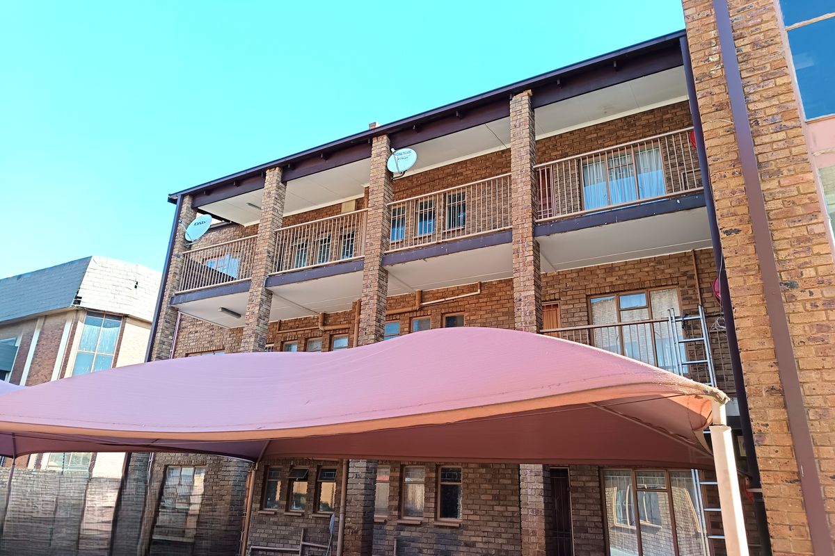 Rear view of a multi-story apartment building featuring face brick construction, private balconies with metal railings, and a large shade sail structure.