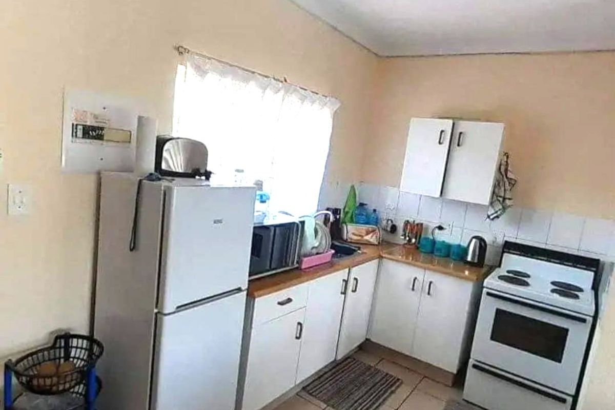 A compact kitchen featuring white cabinetry, laminate countertops, tiled backsplash, and a freestanding stove, offering a functional layout with potential for modernization.