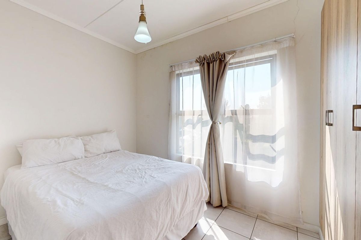 A bright bedroom featuring tiled flooring, a built-in wardrobe, and natural light through a window with sheer curtains.