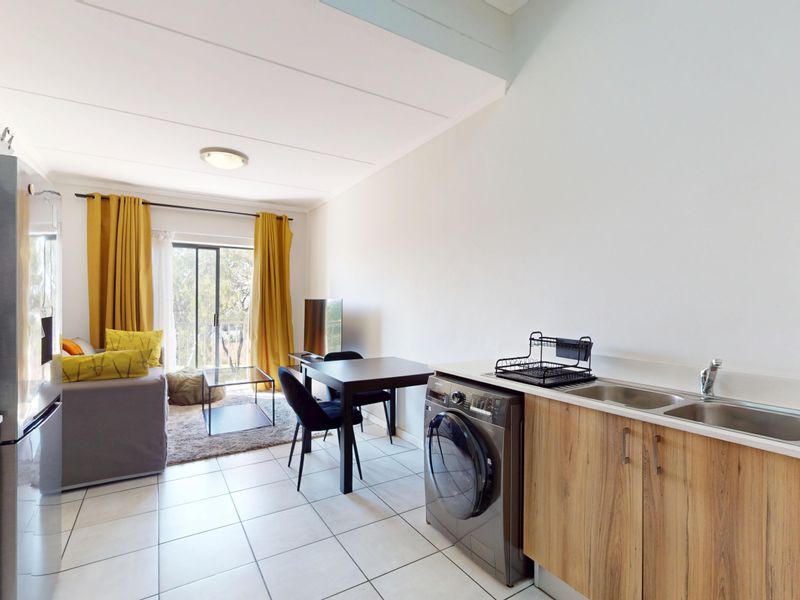 Open-plan living area featuring a compact kitchenette with wood-look cabinetry, stainless steel sink, and direct access to a balcony through sliding glass doors.