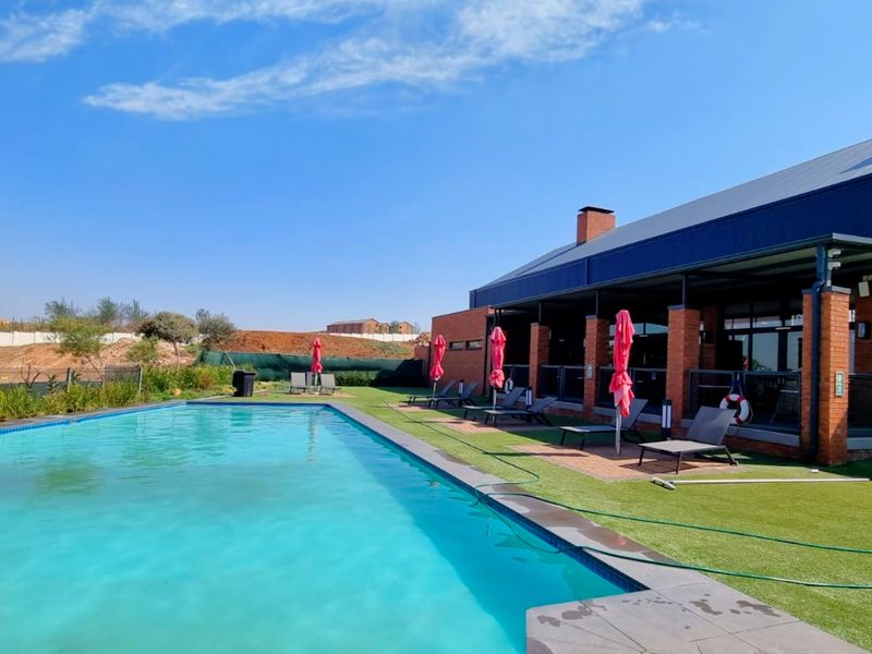 A well-maintained outdoor pool area featuring a swimming pool, artificial lawn, and a covered patio with brick and metal architectural elements.