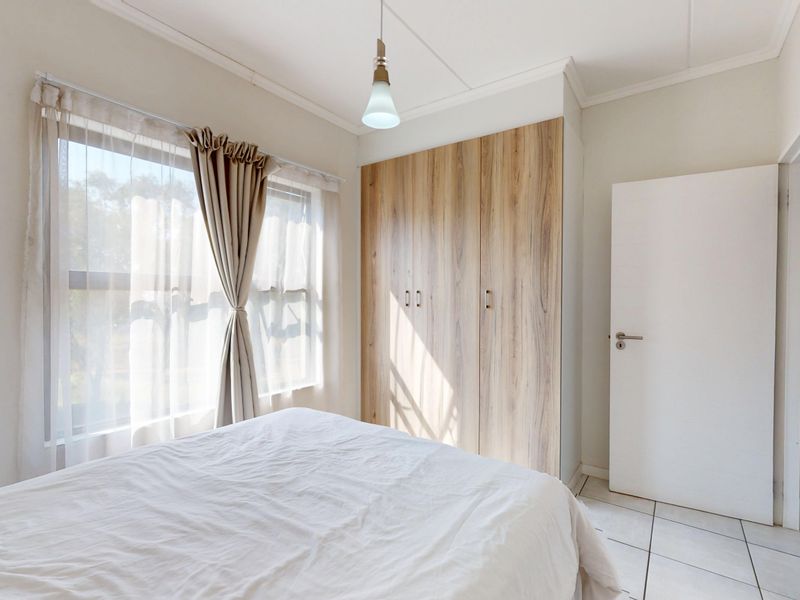 A bright bedroom featuring built-in wooden cupboards, tiled flooring, and natural light through a large window.
