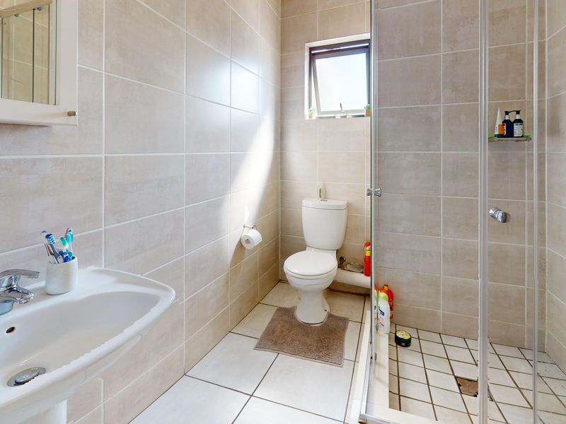 A clean, functional bathroom featuring a pedestal basin, a glass-enclosed shower, and neutral ceramic tiling throughout.