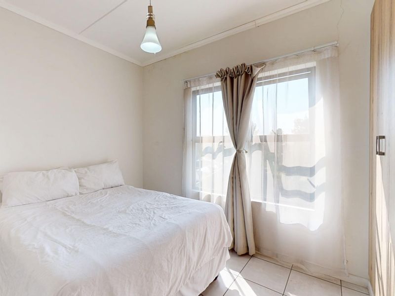 A bright bedroom featuring tiled flooring, a built-in wardrobe, and natural light through a window with sheer curtains.