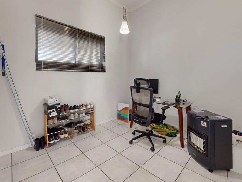 A functional office space featuring tiled flooring, a built-in cupboard, and a window fitted with venetian blinds.