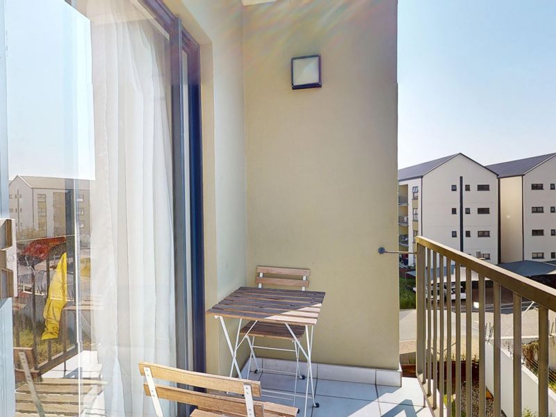 A private balcony featuring tiled flooring, a metal balustrade, and a sliding glass door providing access to the interior living space.
