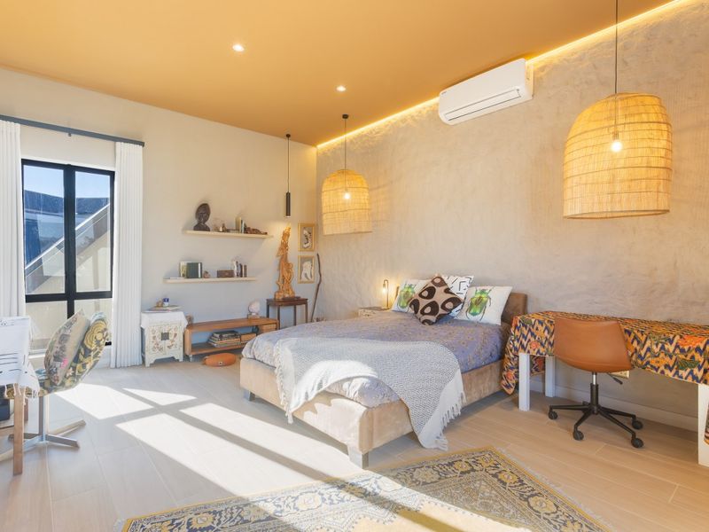 A well-appointed bedroom featuring textured wall finishes, recessed ceiling lighting, integrated air conditioning, and large windows providing natural light.