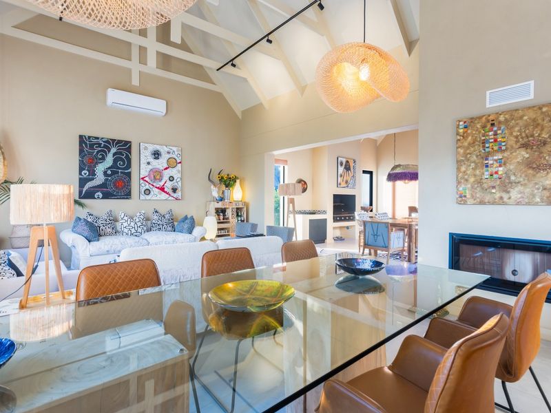 Spacious open-plan living and dining area featuring high vaulted ceilings, exposed trusses, a built-in fireplace, and modern split-system air conditioning.