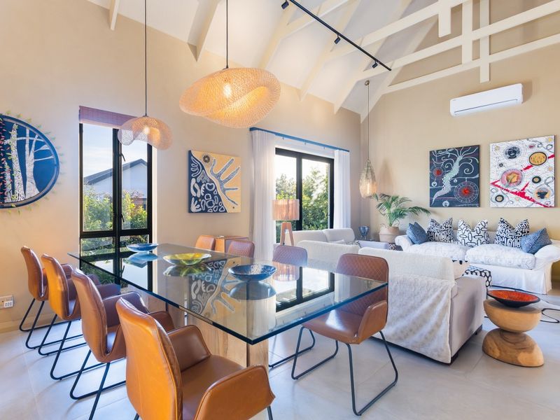 Spacious open-plan living and dining area featuring high vaulted ceilings, exposed beams, large windows, and a wall-mounted air conditioning unit.