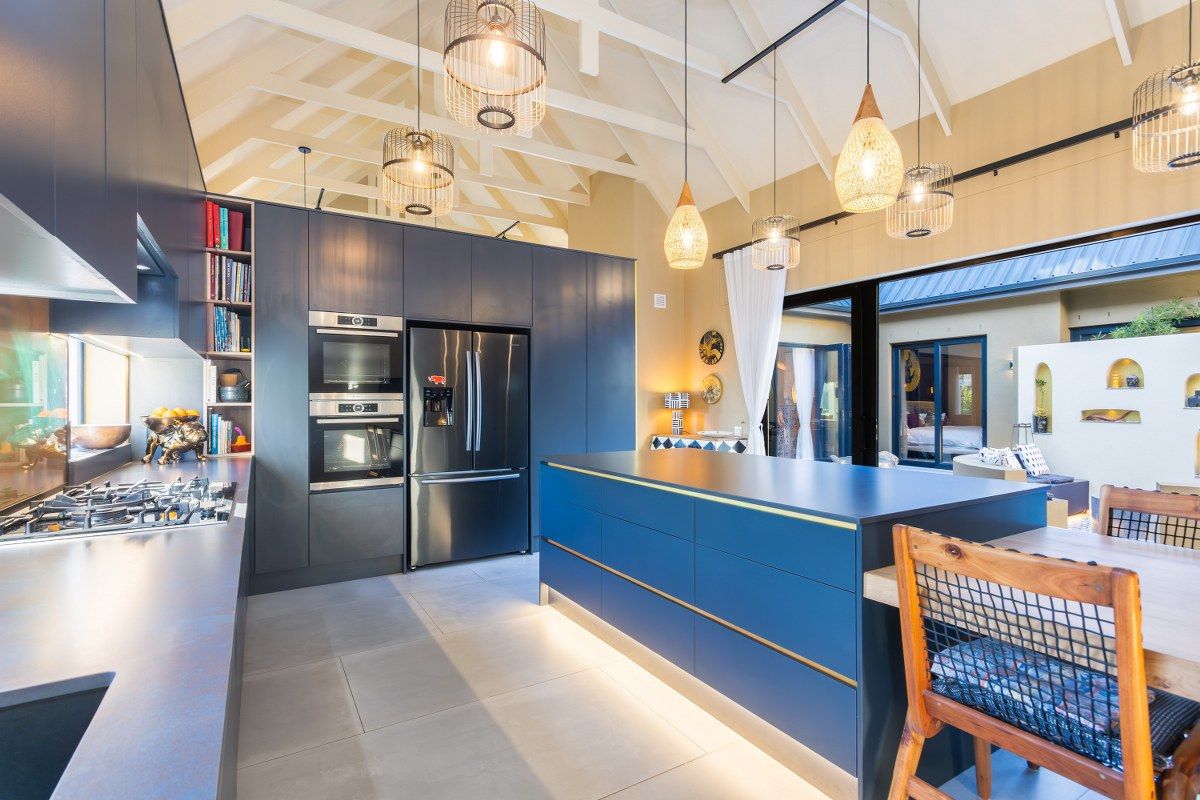 Modern open-plan kitchen featuring dark cabinetry, a large central island, built-in double ovens, gas hob, and vaulted ceilings with exposed beams.