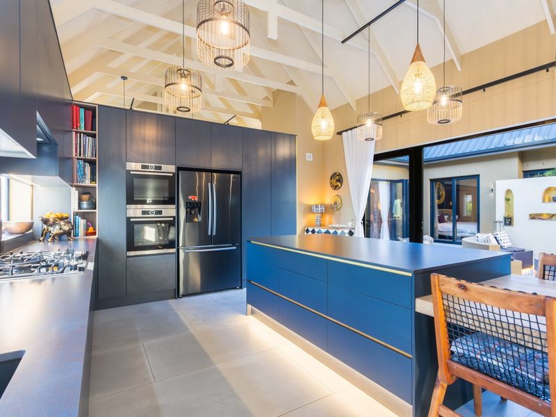 Modern open-plan kitchen featuring dark cabinetry, a large central island, built-in double ovens, gas hob, and vaulted ceilings with exposed beams.