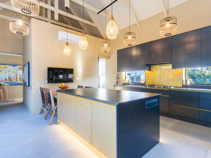 Modern open-plan kitchen featuring a large central island, dark cabinetry, integrated gas cooktop, and high vaulted ceilings with exposed beams.