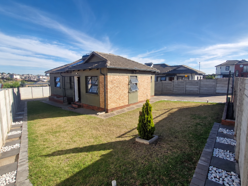 Rear view of a detached house featuring a brick and plaster facade, tiled roof, solar geyser, and a private garden enclosed by precast concrete walls.