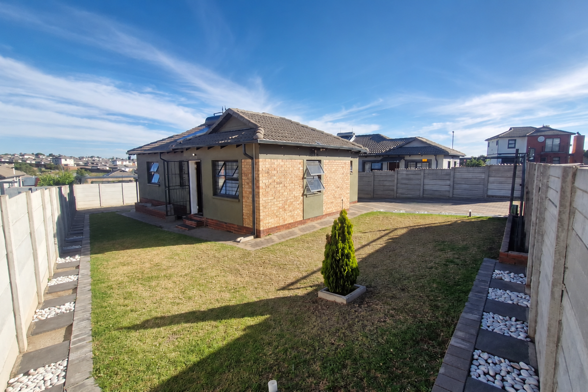 Rear view of a detached house featuring a brick and plaster facade, tiled roof, solar geyser, and a private garden enclosed by precast concrete walls.