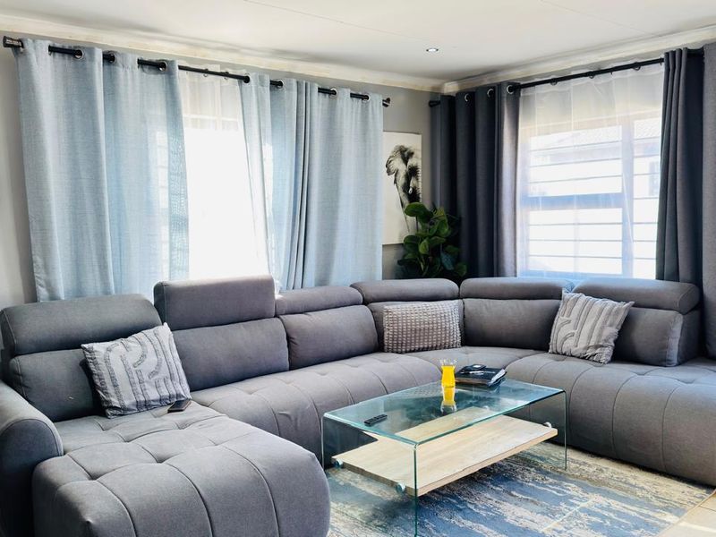 A comfortable living room featuring tiled flooring, recessed downlighting, and large windows dressed with modern curtain rods.