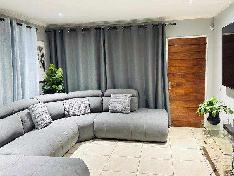 A comfortable living room featuring neutral tiled flooring, recessed downlighting, and a solid wooden door.