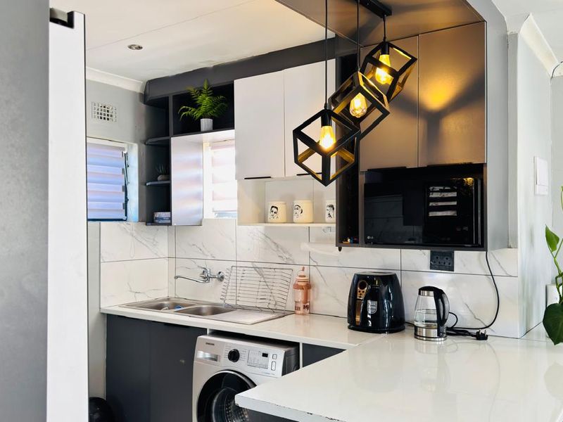Modern kitchen featuring sleek two-tone cabinetry, stone countertops, marble-look tile backsplash, and contemporary pendant lighting with integrated microwave and laundry plumbing.