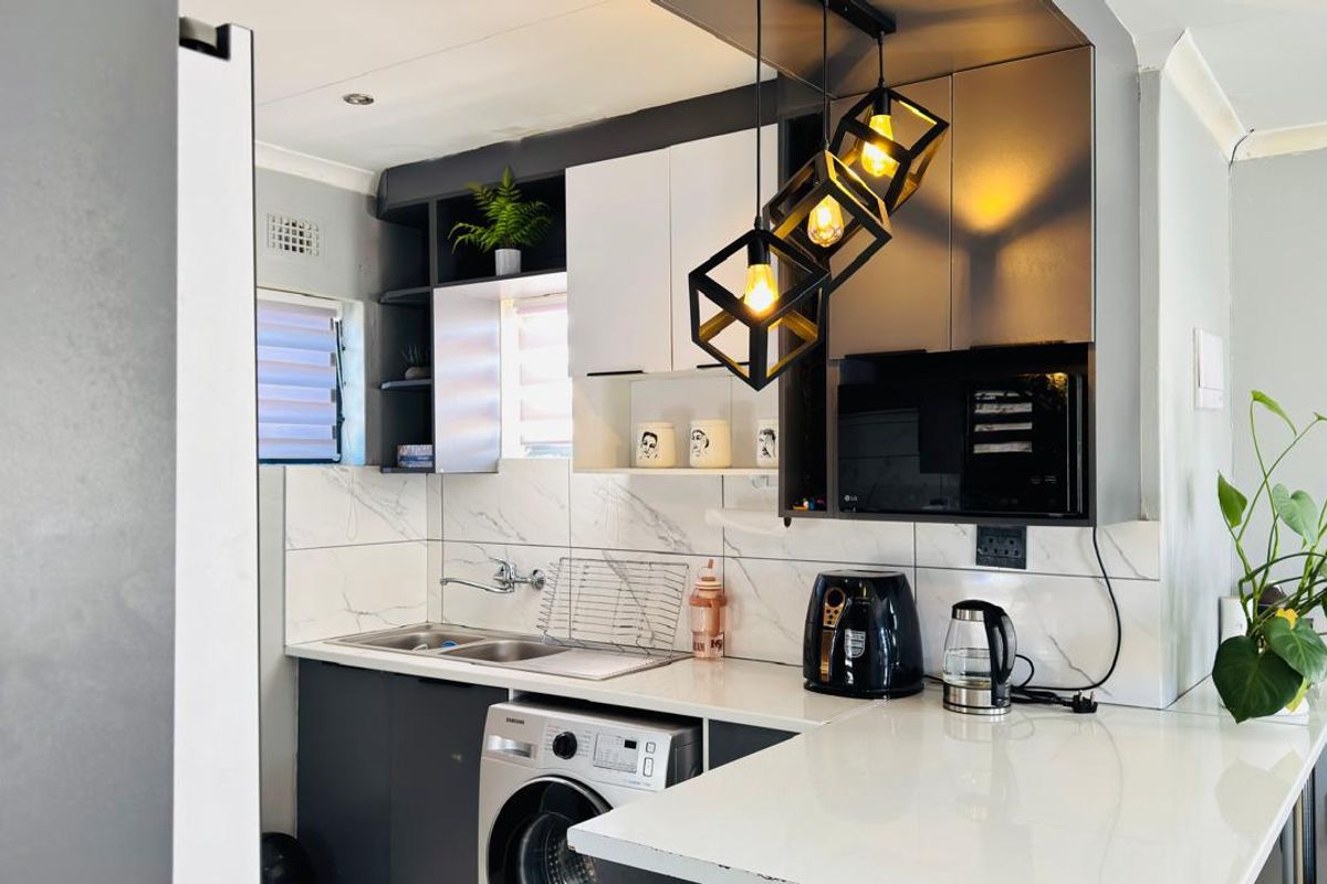Modern kitchen featuring sleek two-tone cabinetry, stone countertops, marble-look tile backsplash, and contemporary pendant lighting with integrated microwave and laundry plumbing.