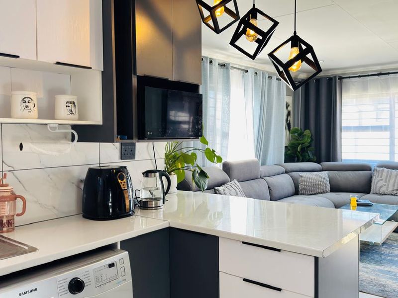 Modern open-plan kitchen and living area featuring sleek two-tone cabinetry, stone countertops, marble-effect splashback, and contemporary geometric pendant lighting.