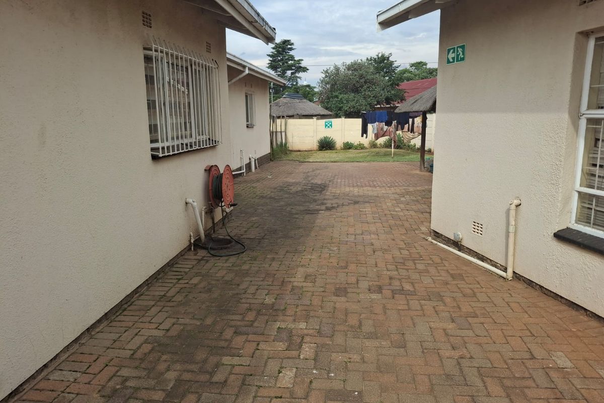 A paved rear courtyard area situated between two building wings, featuring security bars on windows and a perimeter boundary wall.