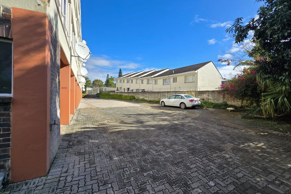 Rear exterior view of the apartment complex featuring a paved driveway, boundary wall, and building facade with mounted satellite dishes.