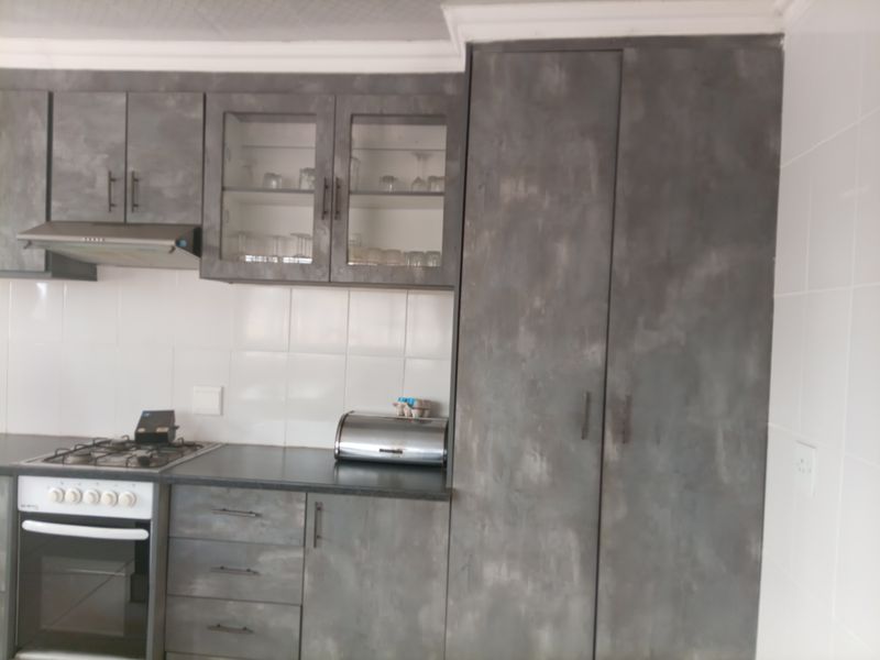 A functional kitchen featuring grey textured cabinetry, a gas hob, built-in oven, extractor fan, and white tiled backsplash.