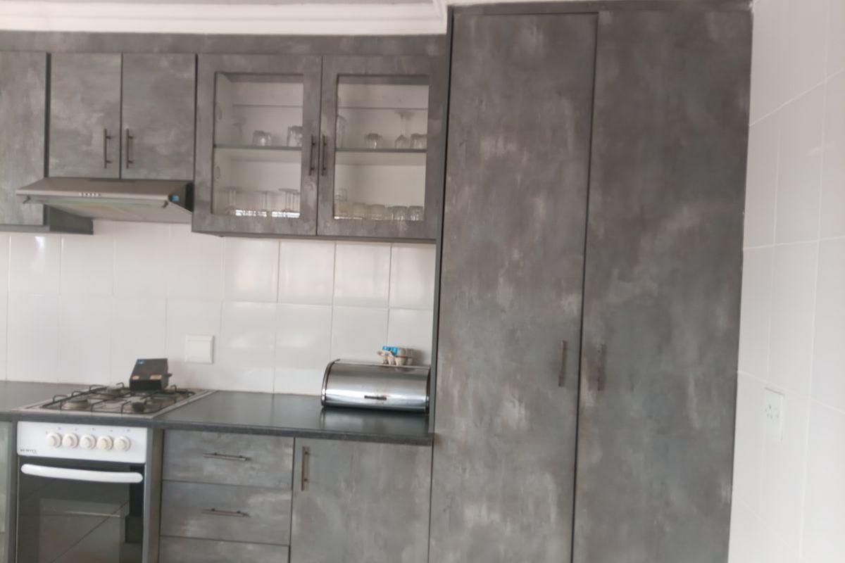 A functional kitchen featuring grey textured cabinetry, a gas hob, built-in oven, extractor fan, and white tiled backsplash.