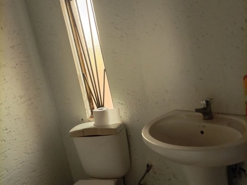 A small bathroom featuring a pedestal basin and toilet with tiled flooring and a vertical window, currently in need of cosmetic refurbishment.