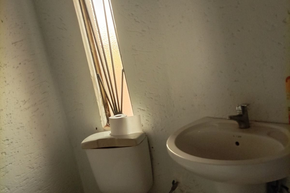 A small bathroom featuring a pedestal basin and toilet with tiled flooring and a vertical window, currently in need of cosmetic refurbishment.