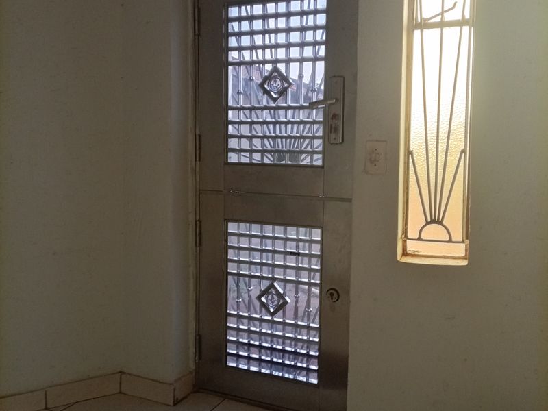 An entrance area featuring a metal security door and a decorative window with tiled flooring.