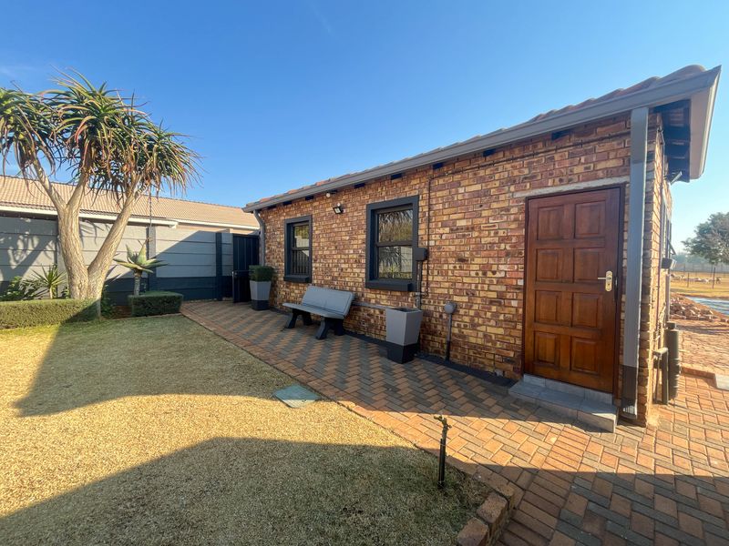 A well-maintained rear exterior view of the cottage featuring face brick walls, a paved patio area, and a solid timber entrance door.
