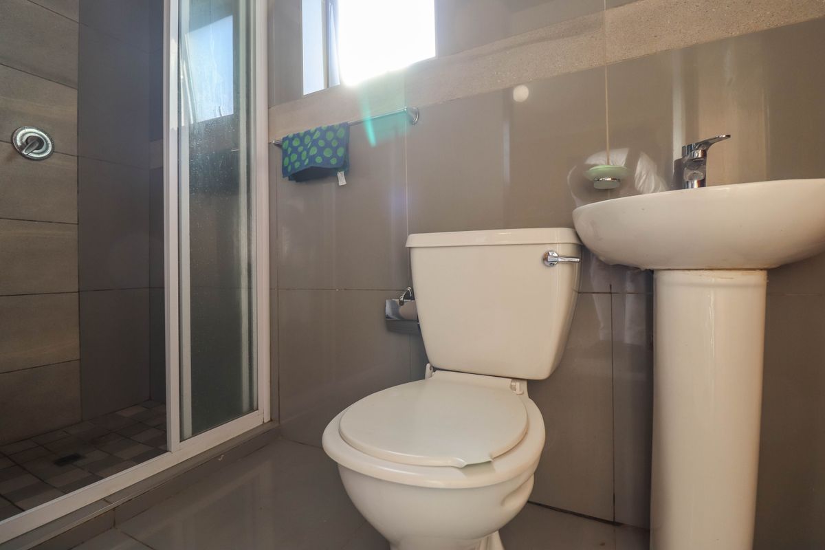 A functional bathroom featuring a pedestal basin, a standard toilet, and a glass-enclosed shower with neutral wall and floor tiling.