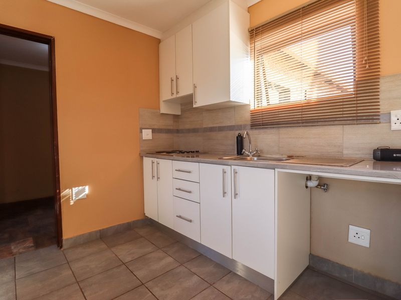 A clean, functional kitchen featuring white cabinetry, tiled backsplash, stainless steel sink, and built-in hob, with neutral wall tones and tiled flooring.