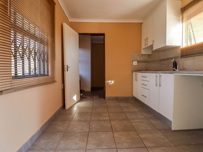 A functional kitchen area featuring white built-in cabinetry, tiled flooring, and a tiled backsplash, offering a clean and practical space.