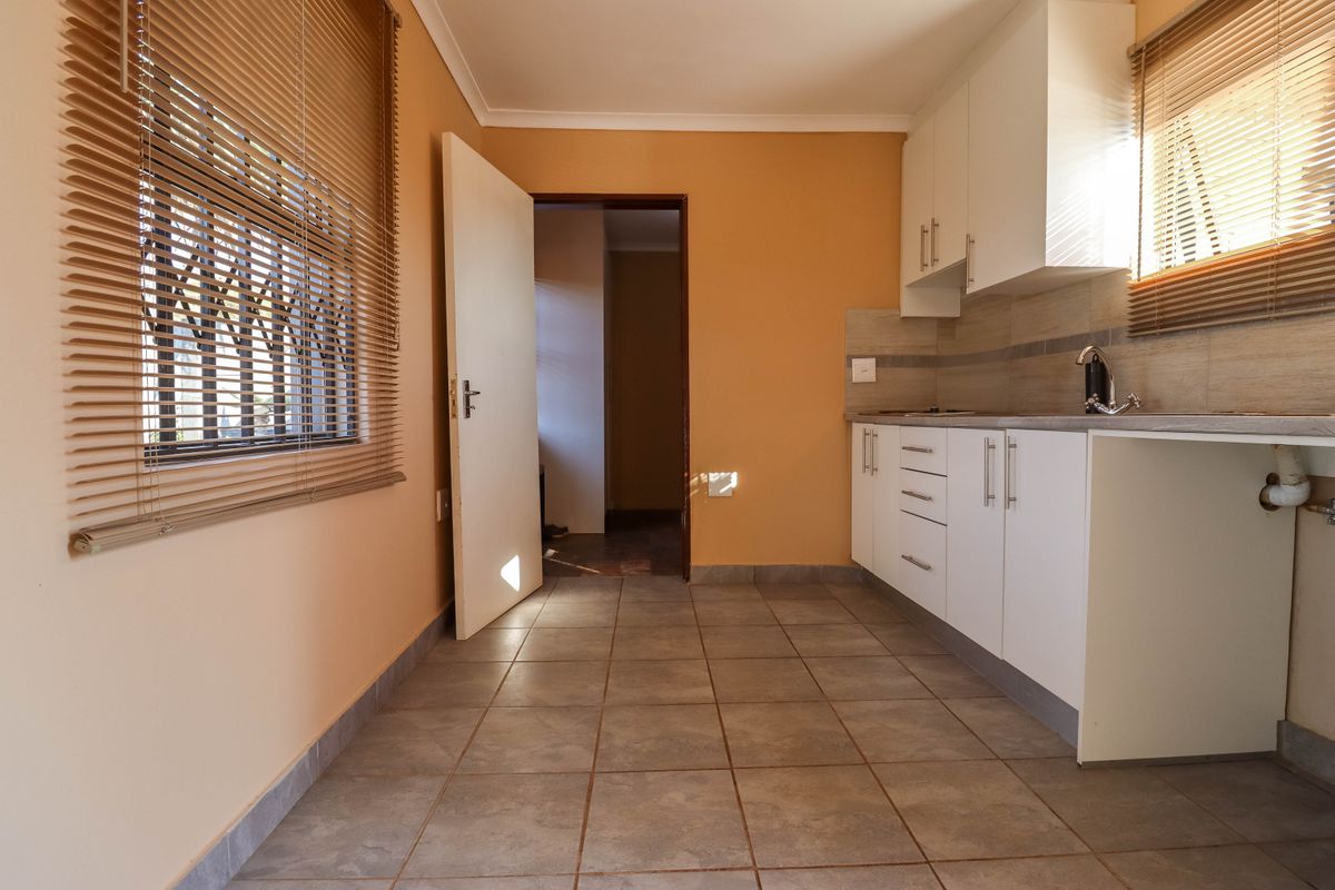 A functional kitchen area featuring white built-in cabinetry, tiled flooring, and a tiled backsplash, offering a clean and practical space.