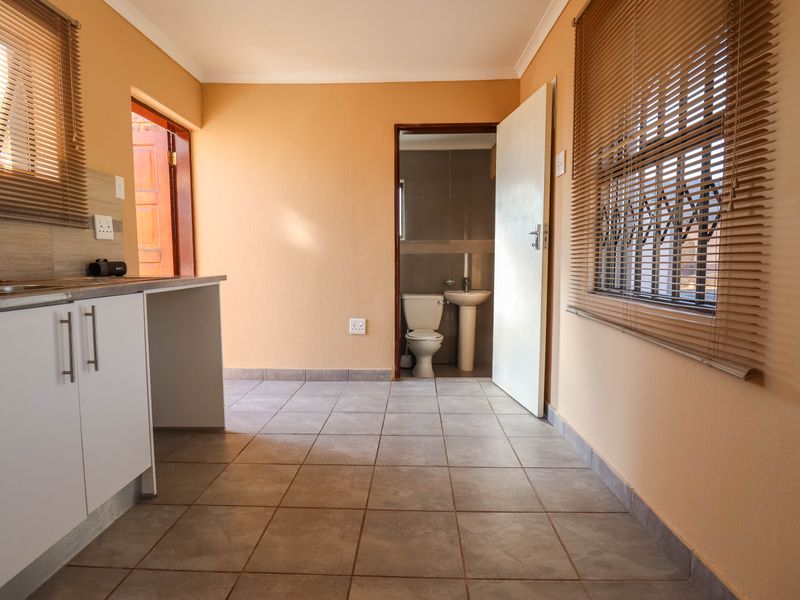 A functional kitchen area with tiled floors and built-in cabinetry, featuring an adjacent bathroom with a pedestal basin and toilet.