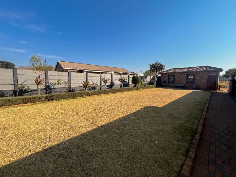 A spacious rear garden featuring a well-maintained lawn, brick-paved pathway, and secure perimeter walling, adjacent to the cottage structure.