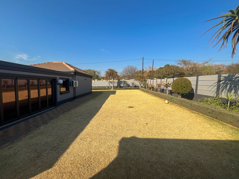 Spacious rear garden featuring a paved patio area, well-maintained lawn, and secure boundary walling, providing a private outdoor space.