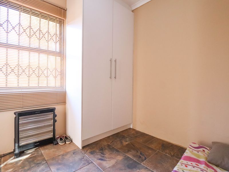 A bedroom featuring built-in white cabinetry, tiled flooring, and a window fitted with security bars and venetian blinds.