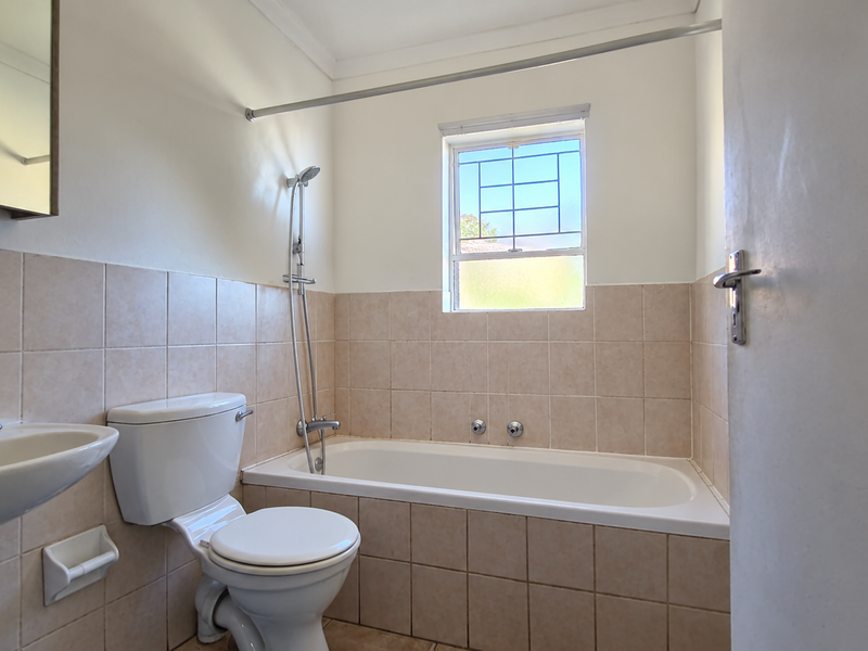 A functional bathroom featuring a pedestal basin, toilet, and a bathtub with a shower mixer, finished with neutral wall tiling.