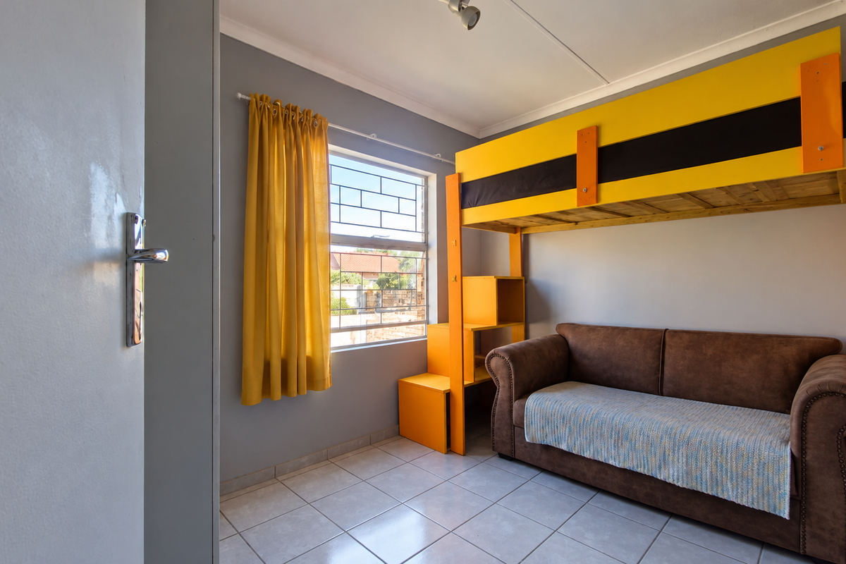 A bedroom featuring tiled flooring and a window fitted with security bars, providing a functional space with neutral wall finishes.
