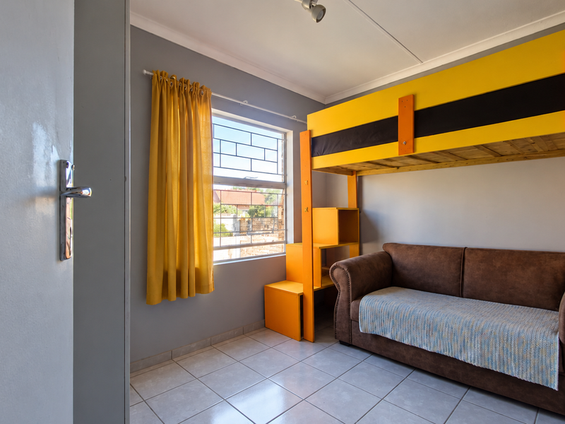 A bedroom featuring tiled flooring and a window fitted with security bars, providing a functional space with neutral wall finishes.