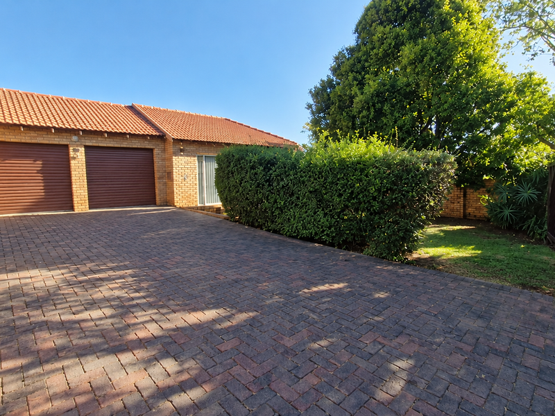 Front exterior view of a townhouse featuring a double garage, brick paved driveway, and well-maintained garden area with mature landscaping.