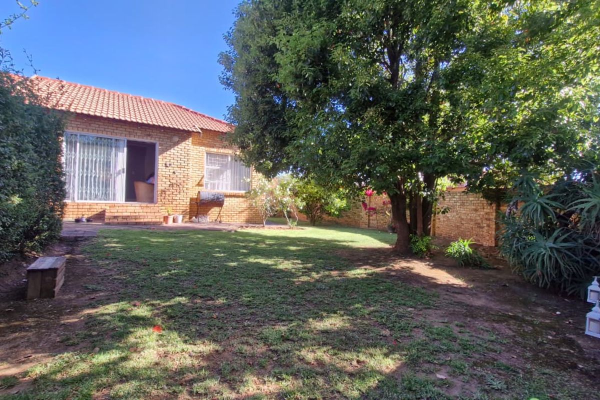 A private rear garden featuring a face brick townhouse facade, mature trees, and a lawn area with perimeter walling.