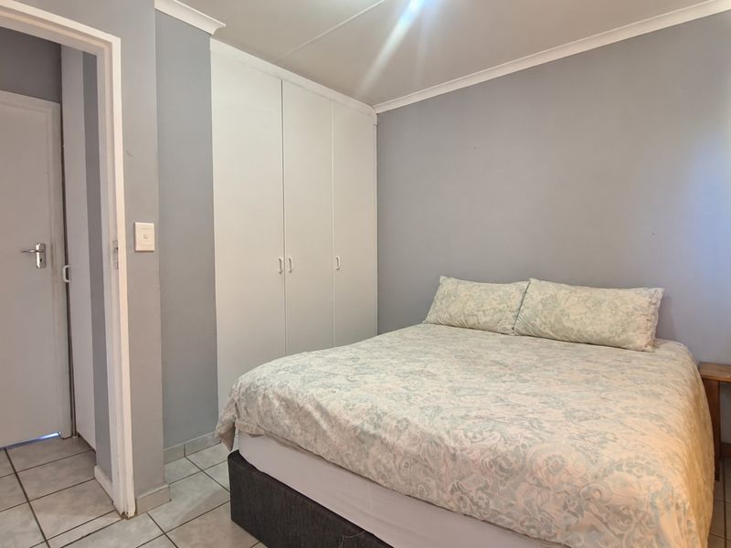 A functional bedroom featuring built-in cupboards, tiled flooring, and neutral wall finishes, providing a clean and practical living space.
