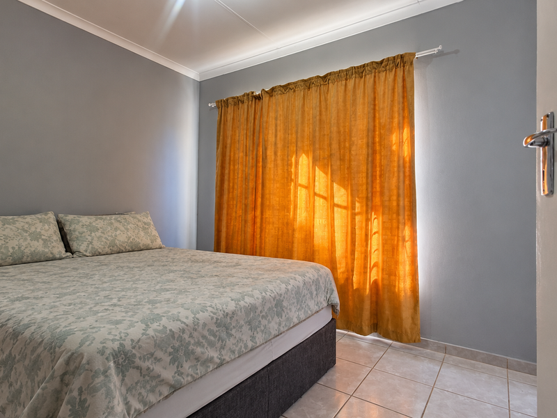 A bedroom featuring tiled flooring and neutral grey walls, illuminated by natural light through window curtains.